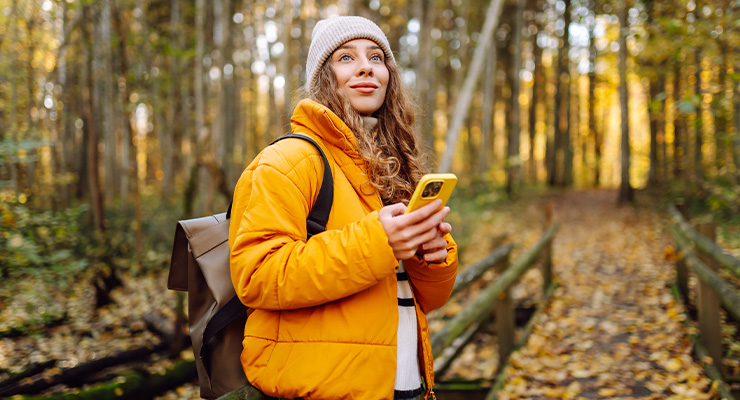 Persoon wandelt in een herfstbos en gebruikt een smartphone