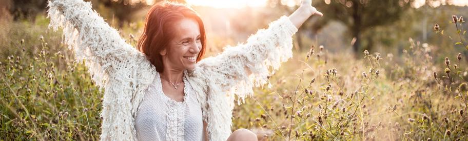 Vrouw lacht ontspannen in een veld bij zonsondergang
